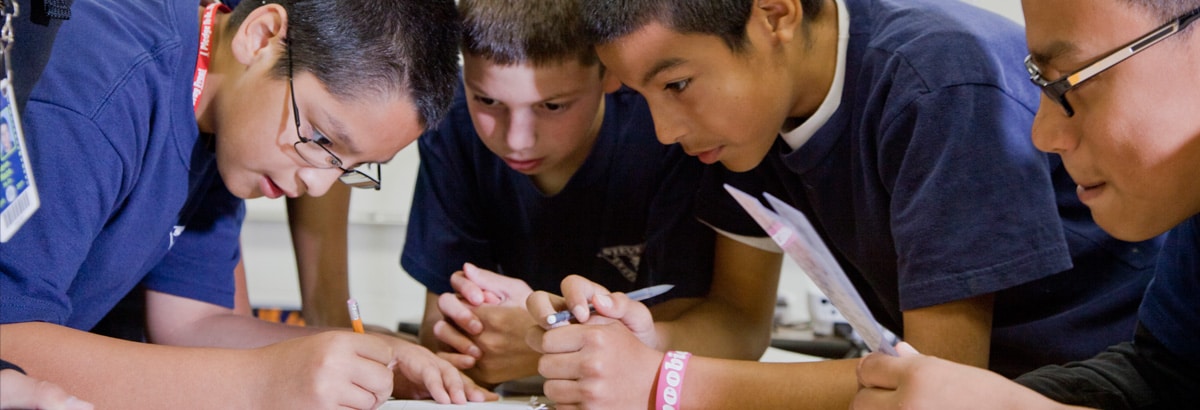 Students taught by a Teach For America teacher huddle around to work on a project.