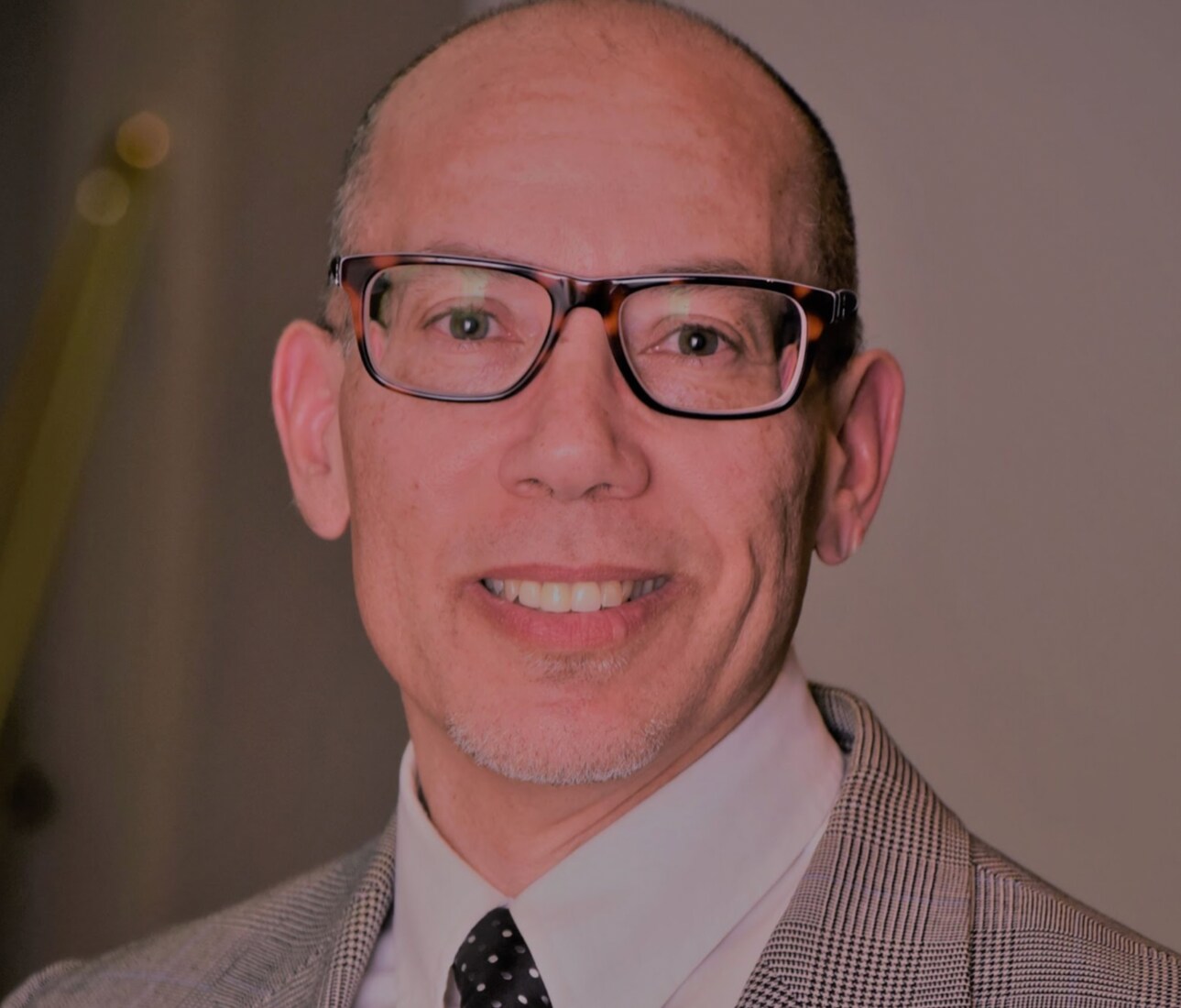 A man wearing glasses and a collared shirt with a tie and beige jacket.