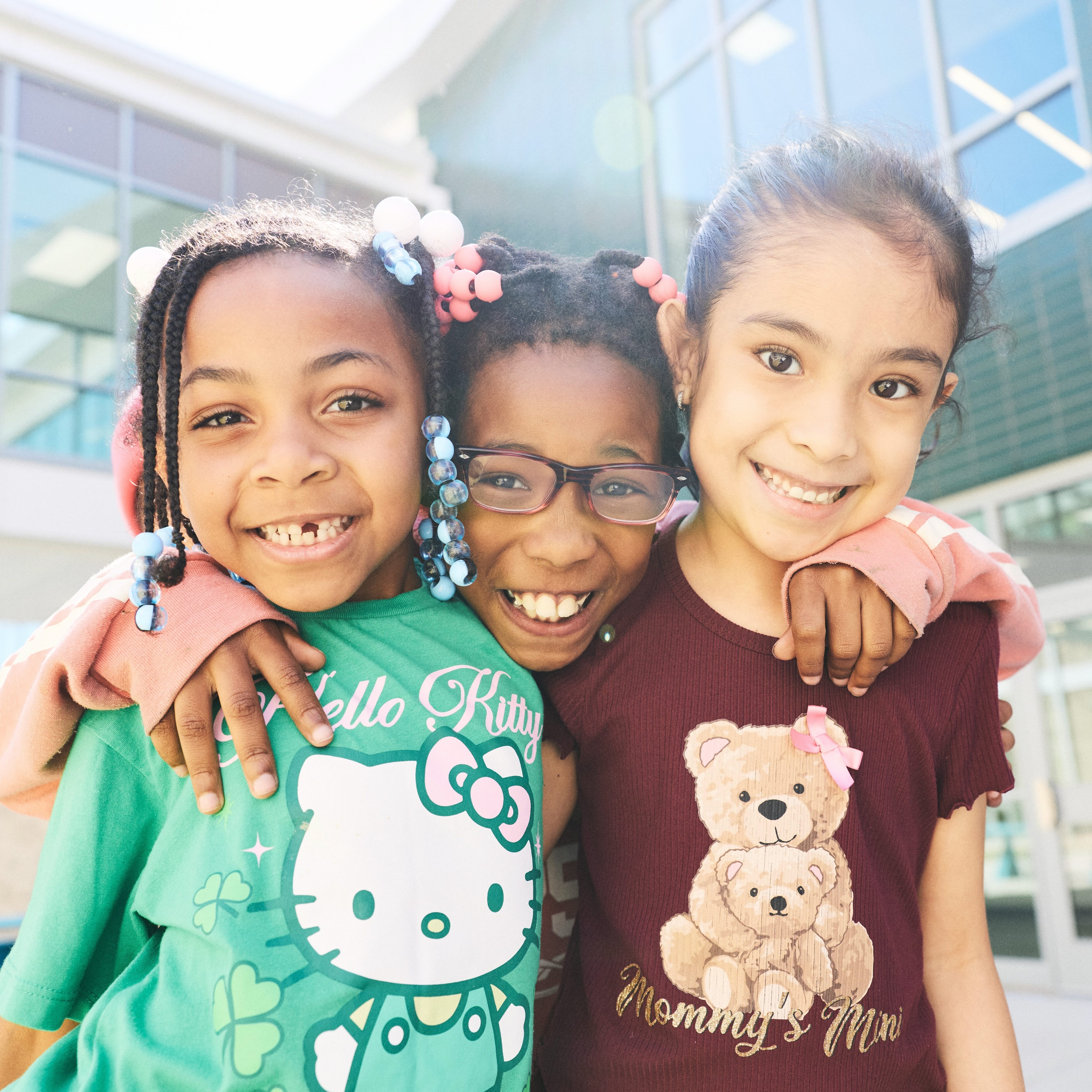 A student putting her arm around two friends on the playground.