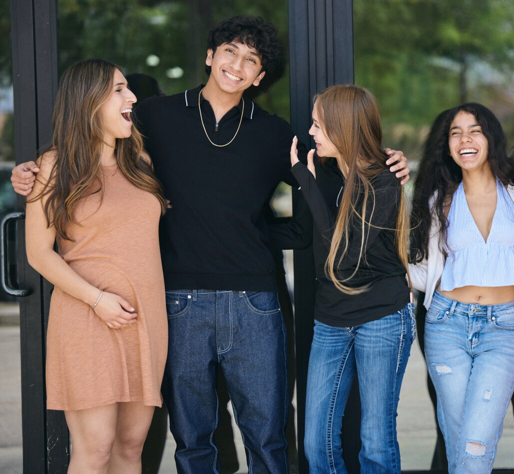 Teachers embrace and smile outside of a school.