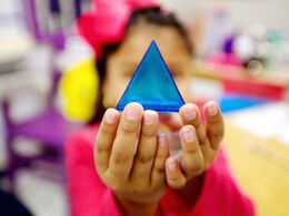 A young student holding a small clear blue pyramid.