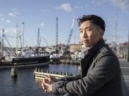 A man looks out over a harbor with boats in the background