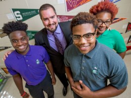 A man stands with three students. Everyone is smiling.
