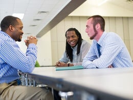 three men sitting at a table and talking to one another