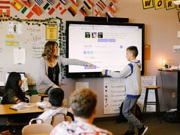 Alt text: a teacher is helping a student understand a lesson projected on a tv screen.