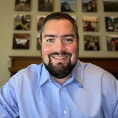 A man with a beard. He is wearing a blue button up shirt.