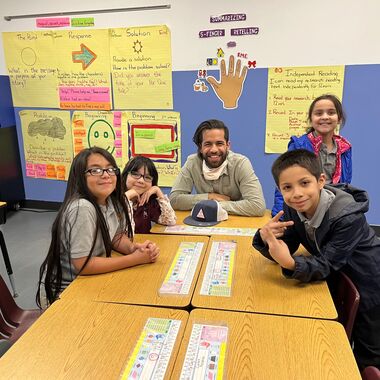 A teacher sits a classroom table with four students