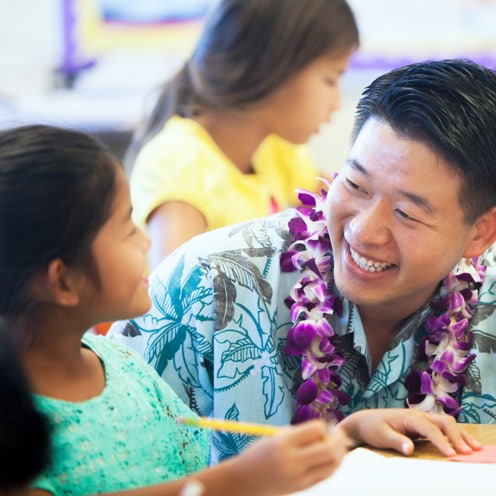 A teacher smiles at a student while they work together.