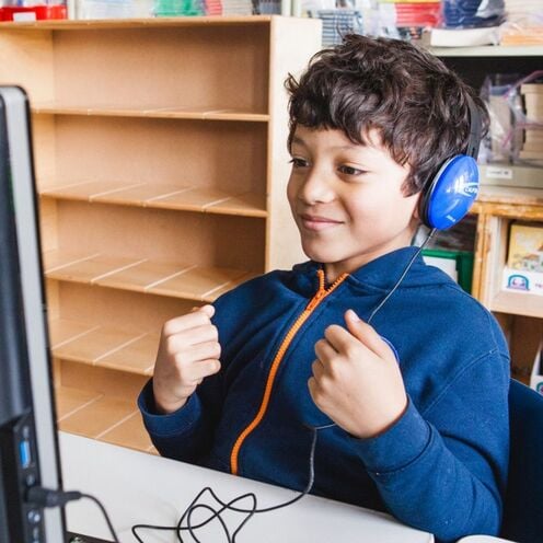A student with headphones interacting with a computer.