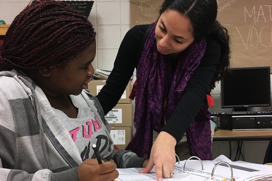 A Teach For America teacher working with a student at her desk.
