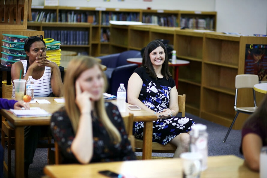 Three women sit in a school library watching a presentation