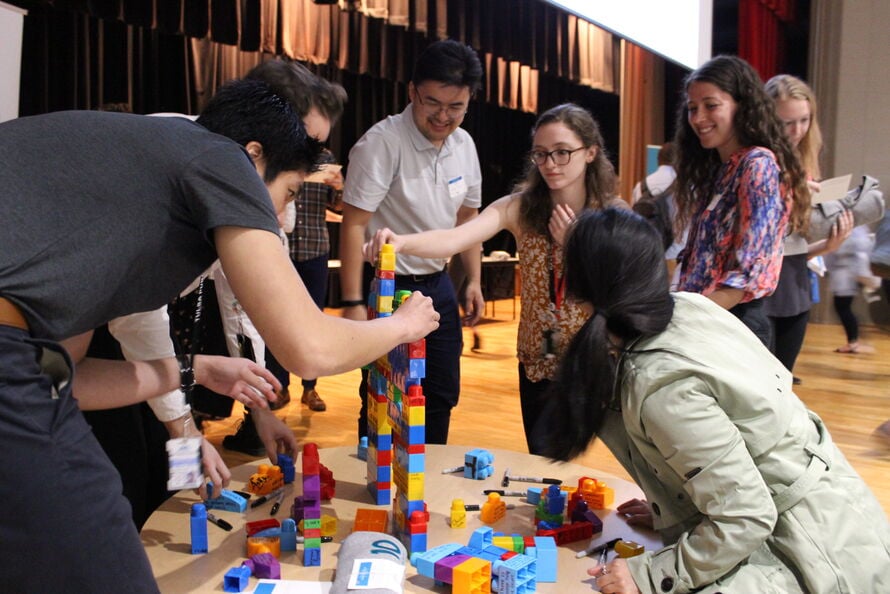 Group of various adult individuals around a round table putting together building blocks