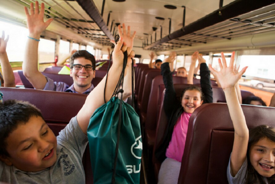 Kids on a bus with hands raised