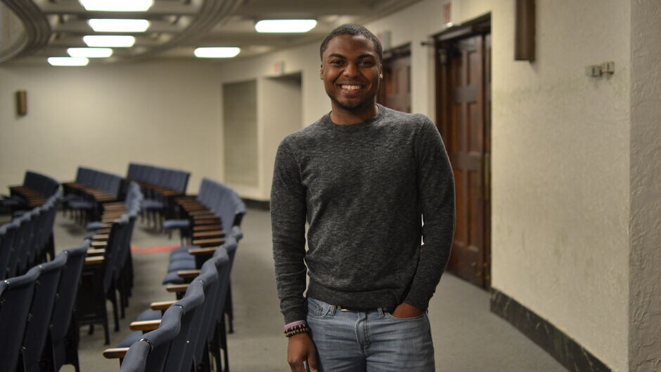 A male corps member stands in an auditorium.