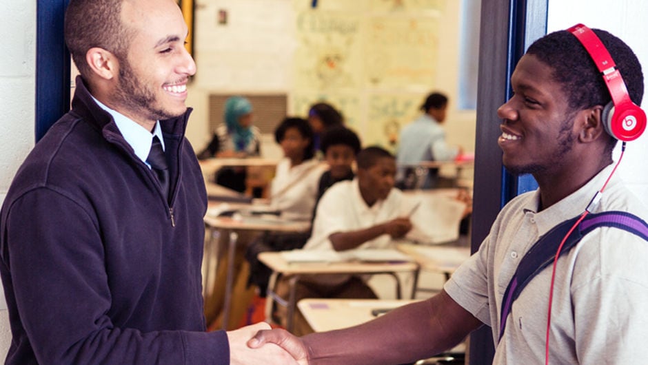 A teacher gives a student a high-five at the classroom entrance.