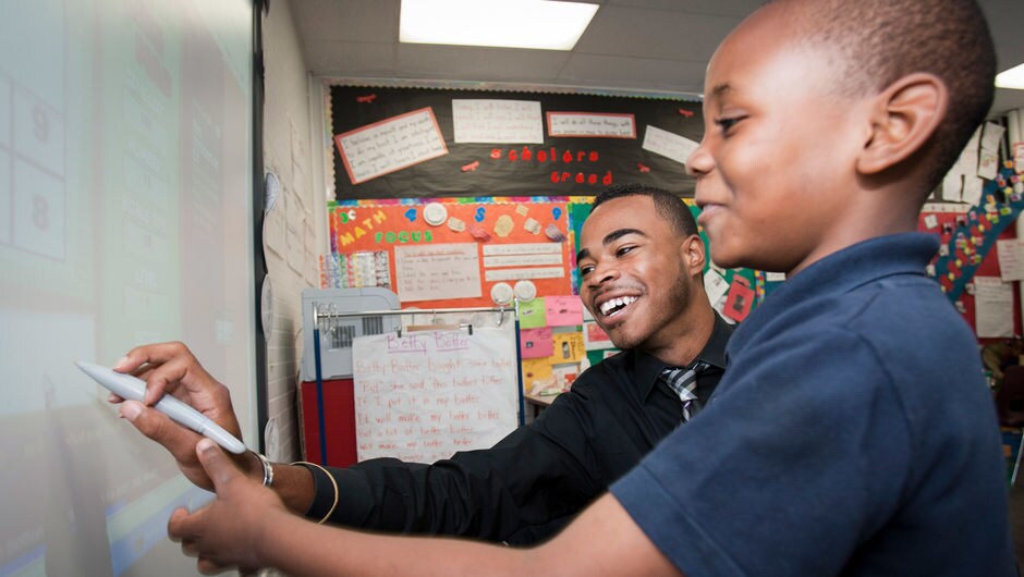 A teacher helps a student at the whiteboard.