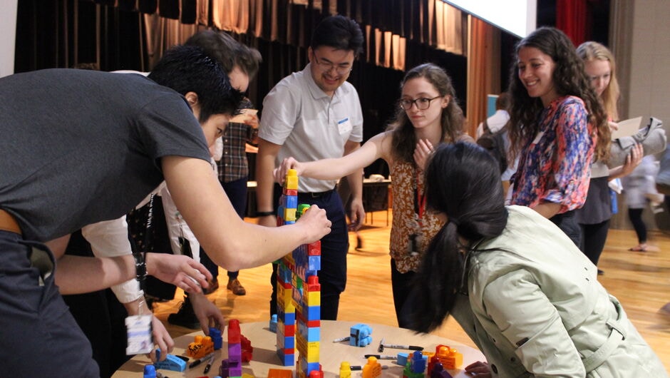 Group of various adult individuals around a round table putting together building blocks