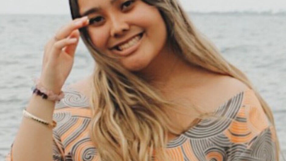 A photo of a young woman with the ocean behind her. 