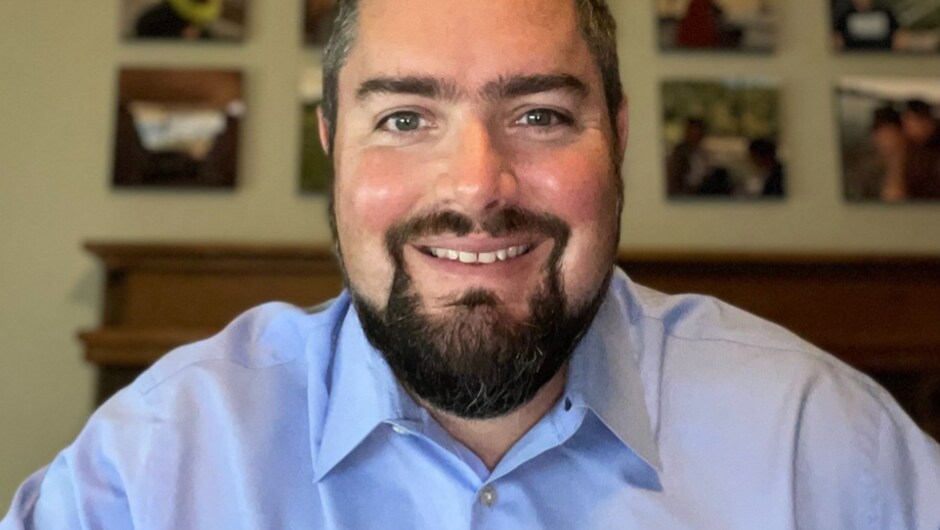 A man with a beard. He is wearing a blue button up shirt.