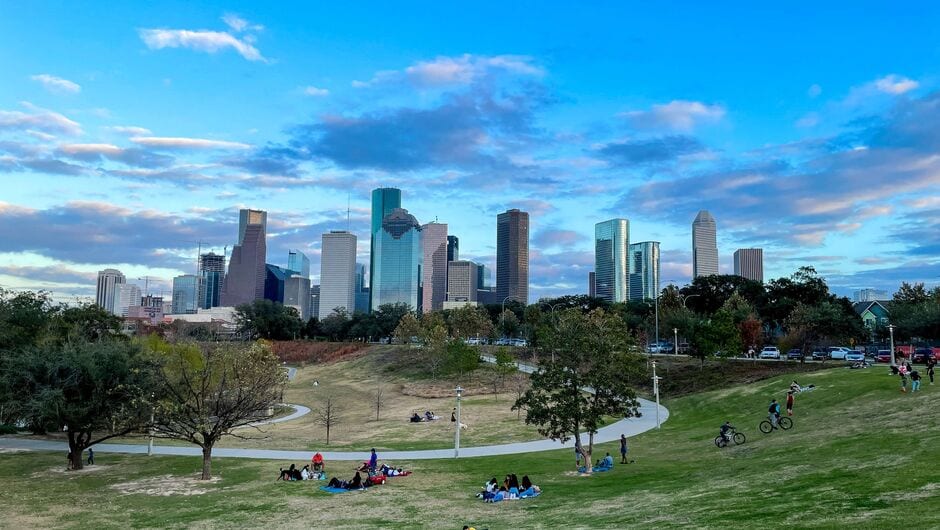 A view of the Houston skyline with picnicers on a grassy hill in the foreground.