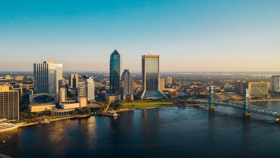 A skyline of Jacksonville with a body of water and bridge in the foreground.