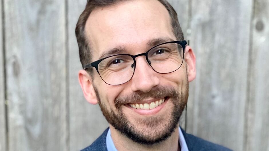 Portrait of Ryan Pavel wearing glasses, light blue shirt and dark blue jacket.