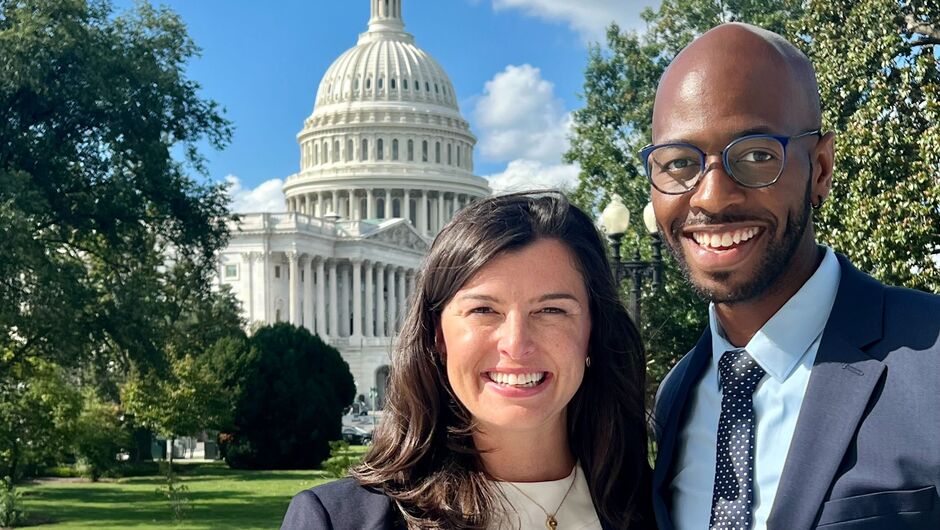 Two people stand together in front of Capitol Hill 