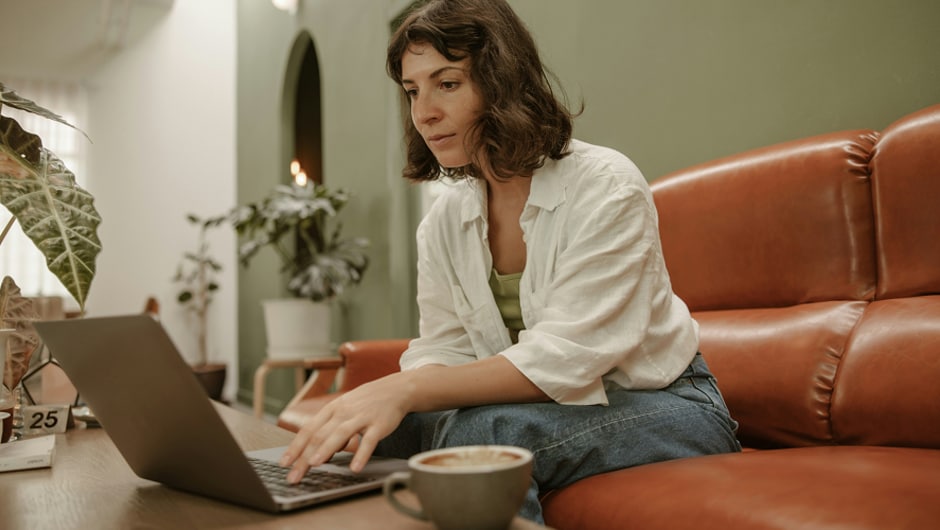 A young woman sitting on a couch, working on a laptop.
