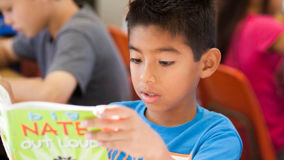 A young student reading a book in class.