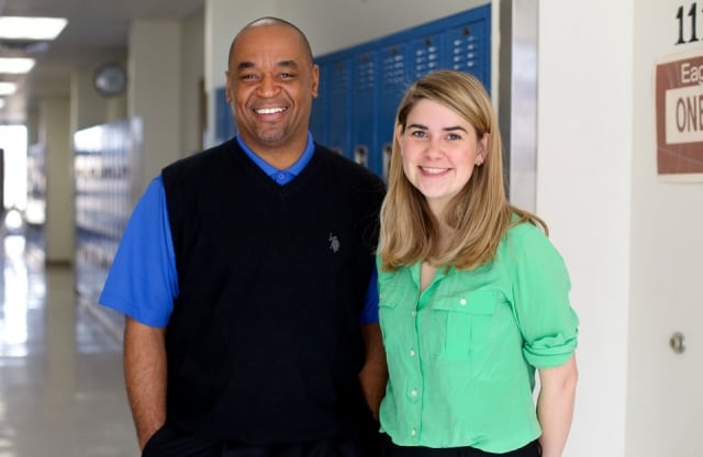 A principal and teacher standing together in a school hallway.