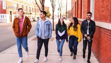 A group of young adults walks down a sidewalk together smiling