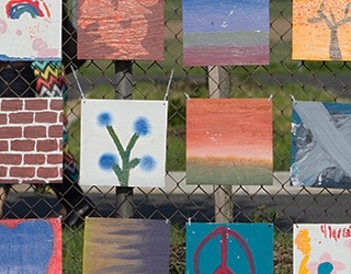 A mural of canvasses displaying student artwork hang on a fence.