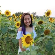A photo of Serena Puang smiling in a field of sunflowers.