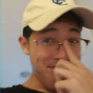 A photo of a young man wearing a tan hat pushing up the bridge of his glasses.