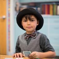 a young boy wears a black hat, a great vest, a dark grey shirt, and a bow tie.