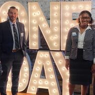 Four Teach For America alumni stand next to a One Day display