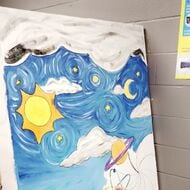 Three students paint stars, a moon, and a sun on a canvas
