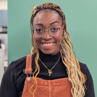 women with blonde braids smiling in front of a green wall