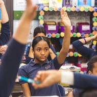 Students raise their hands in a classroom.