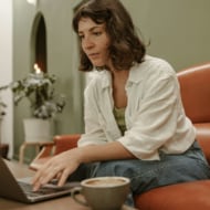 A young woman sitting on a couch, working on a laptop.